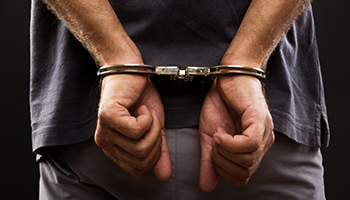 A close-up view from behind of a person’s hands secured in metal handcuffs.